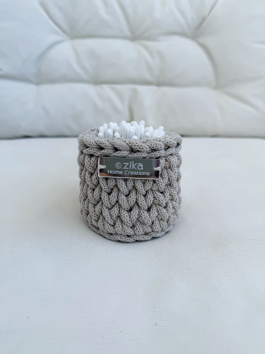 Close-up detail of the rustic texture, silver logo tag, and woven stitching on a small handcrafted cotton basket.